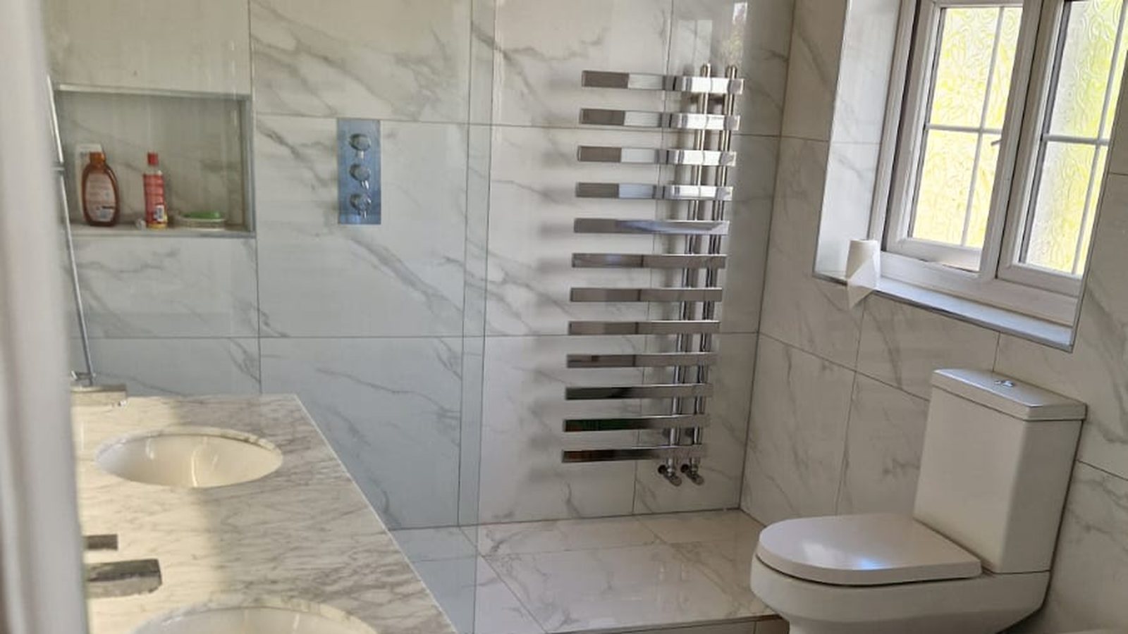 Marble family bathroom with twin basins and walk-in shower by AG Signature Renovation