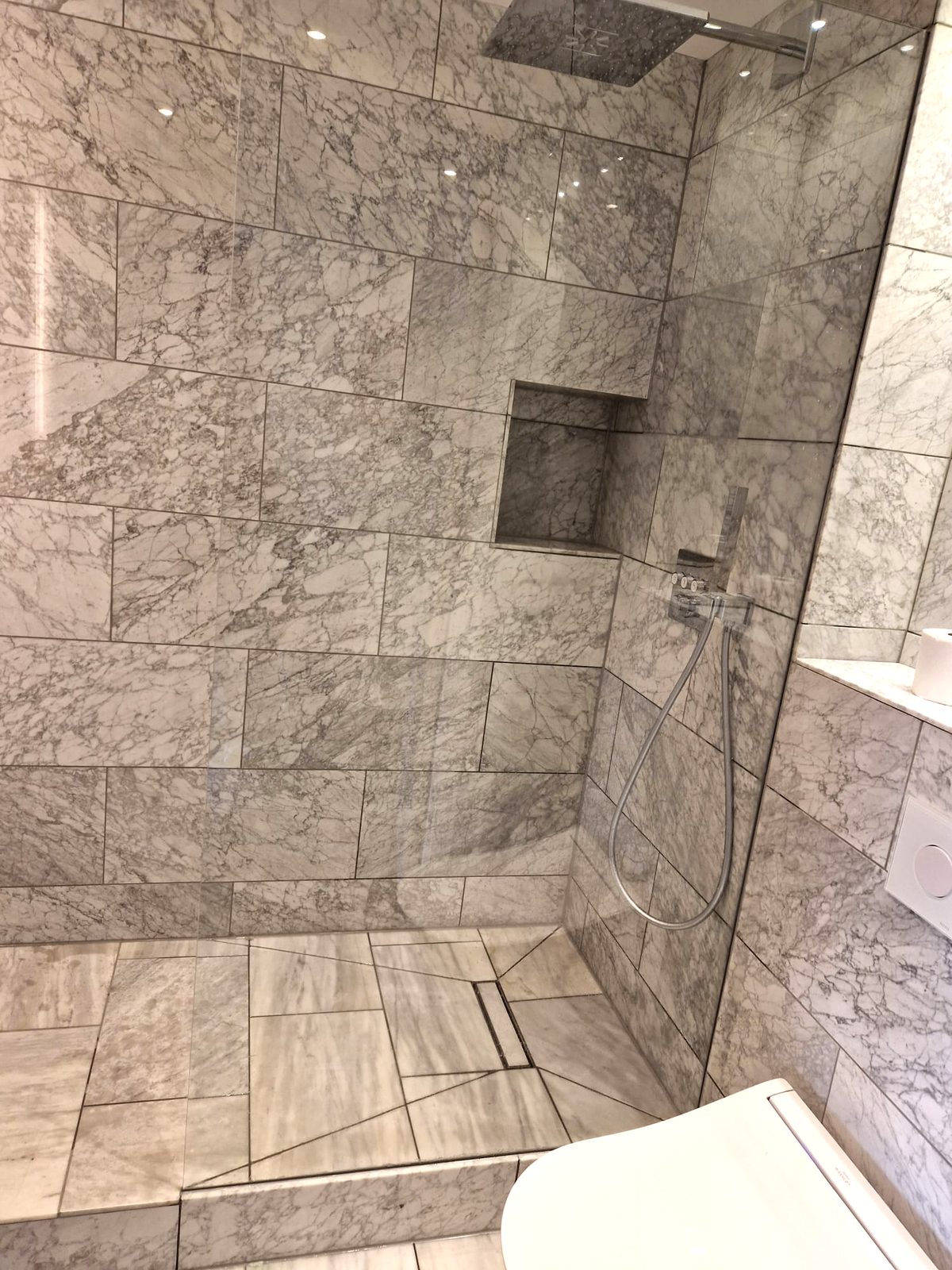 Marble walk-in shower with recessed shelf by AG Signature Renovation